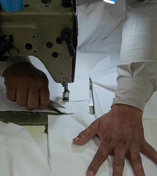 Hands finishing a white BJJ gi at a sewing machine